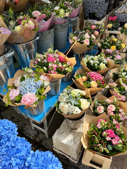 A display of freshly arranged floral bouquets on a blue table, featuring a variety of flowers including pink roses, white and green lisianthus, soft blue hydrangeas, and delicate pink carnations, all